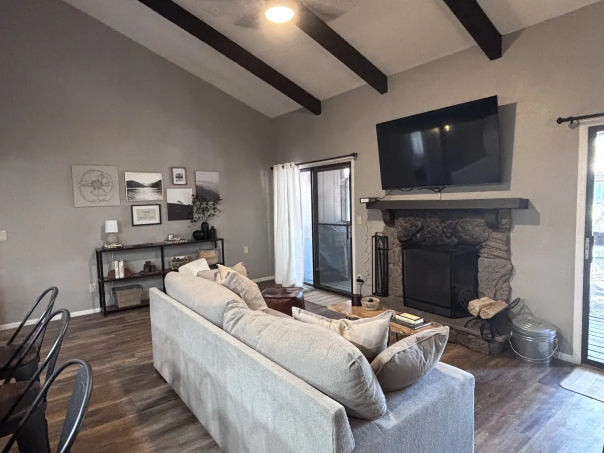 A spacious great room is anchored by a large sectional sofa facing a cozy fireplace and TV, with a dining area and direct access to the outdoors via a sliding glass door. The furnishings invite relaxation and conversation, while the layout emphasizes both comfort and connection.