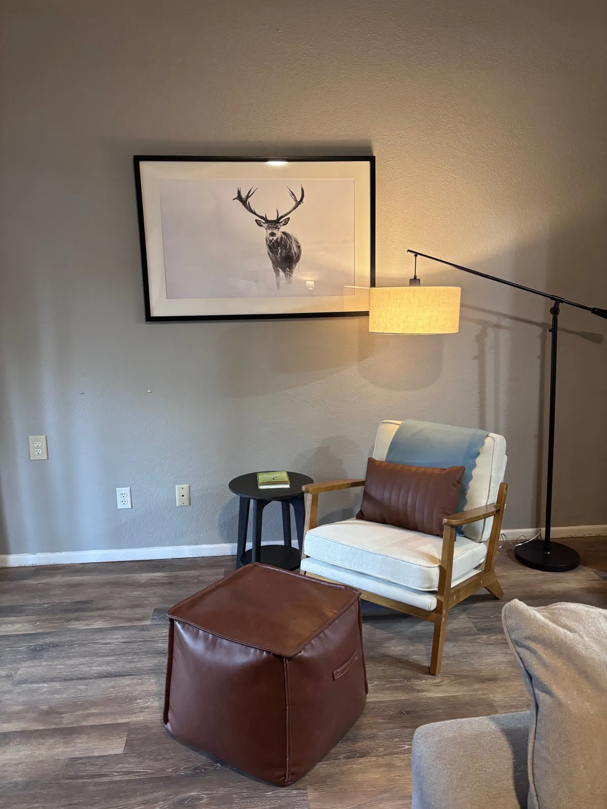 A tranquil corner with a comfortable armchair, framed deer artwork, a floor lamp, ottoman, and a side table with a book. The setting is serene and ideal for savoring quiet moments, with decor that brings the forested environment inside.