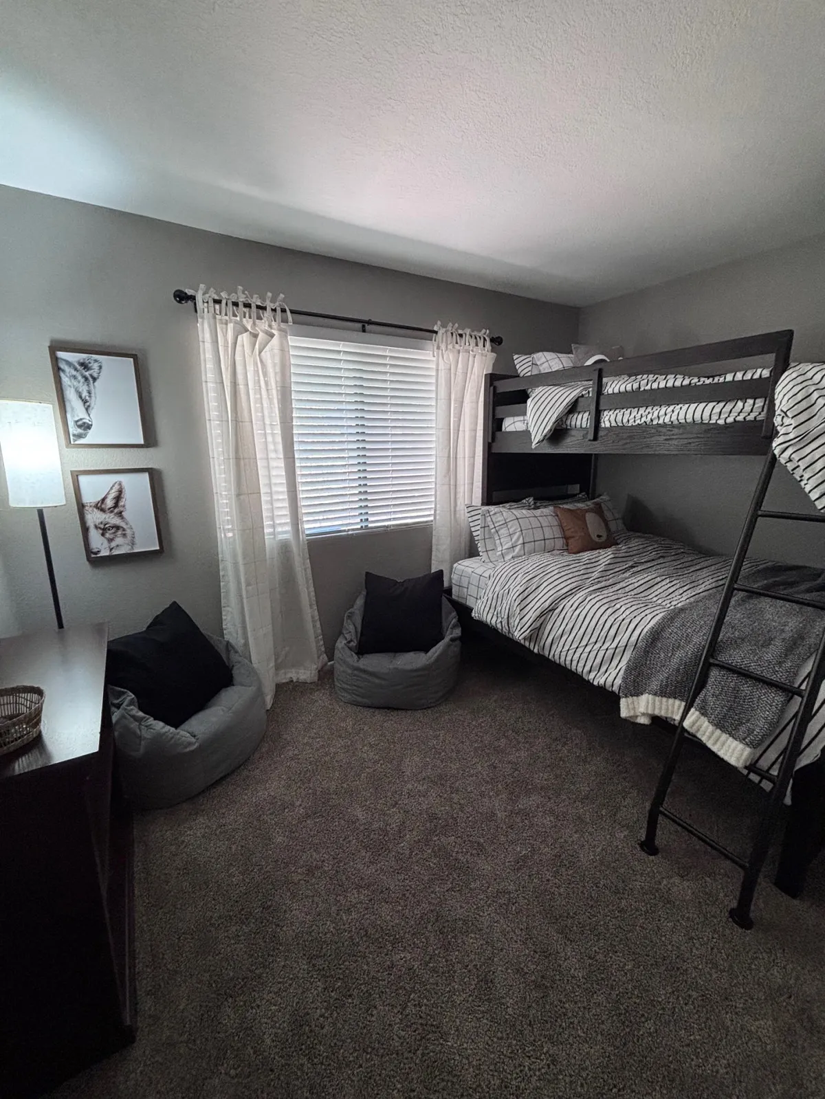 This image centers on a bedroom with a twin over full bunk bed, bean bag chairs, playful artwork, and a lamp. The space is well-lit by daylight, with bean bags inviting lounging, playing, or storytime. The youthful decor and relaxed seating make it ideal for kids or groups of friends.
