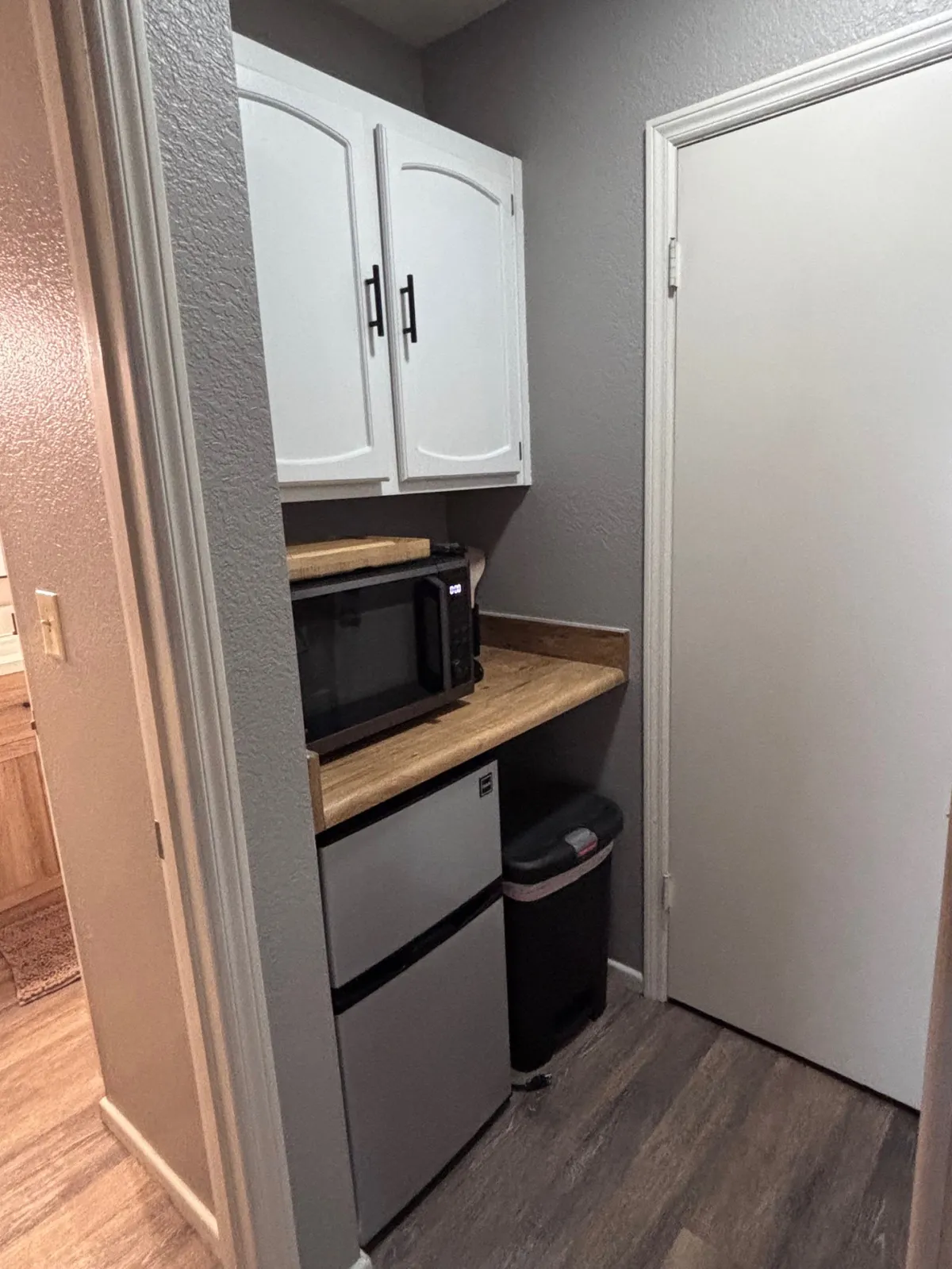 A compact kitchenette setup with a microwave, mini fridge, wooden countertop, and white cabinets is showcased here. The space is practical and efficient, ideal for preparing quick snacks or enjoying a morning coffee in privacy.