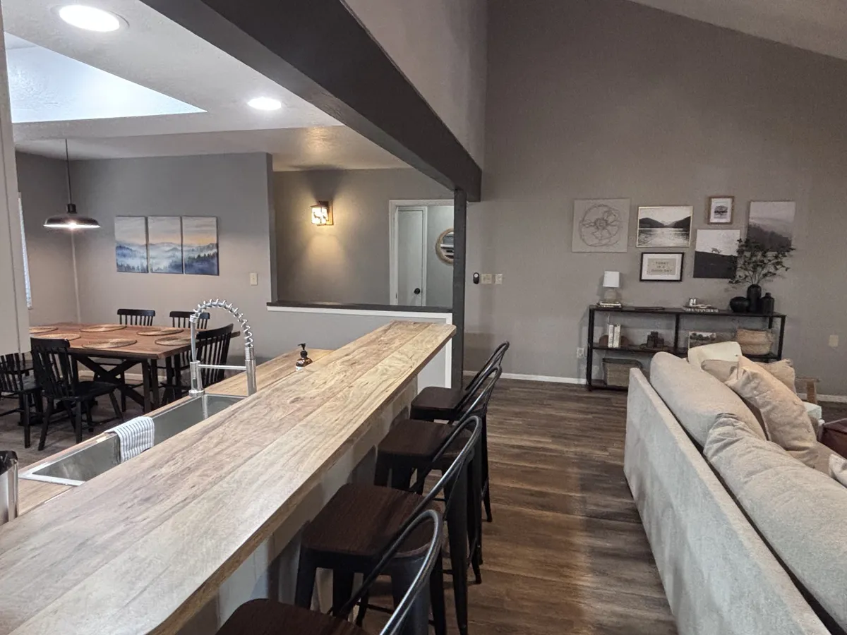 A warm, welcoming interior featuring a modern kitchen island, an adjacent dining table, and a comfortable seating area. Art adorns the walls, and the open layout allows for effortless transitions between cooking, dining, and socializing.