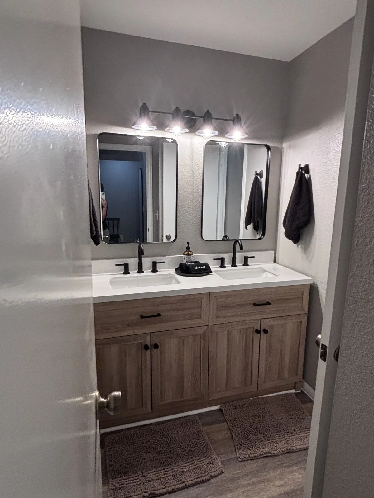 A bright, organized bathroom with double sinks, mirrors, and modern lighting fixtures. Wooden cabinetry adds warmth, and the layout supports simultaneous use by multiple family members. The space feels serene and functional, perfect for morning and evening routines.
